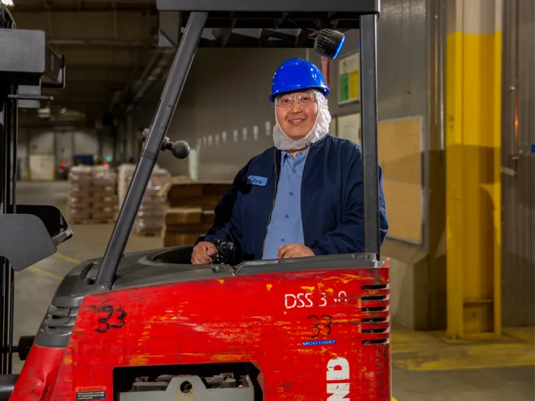 Woman wearing a hard hat standing in front of a forklift