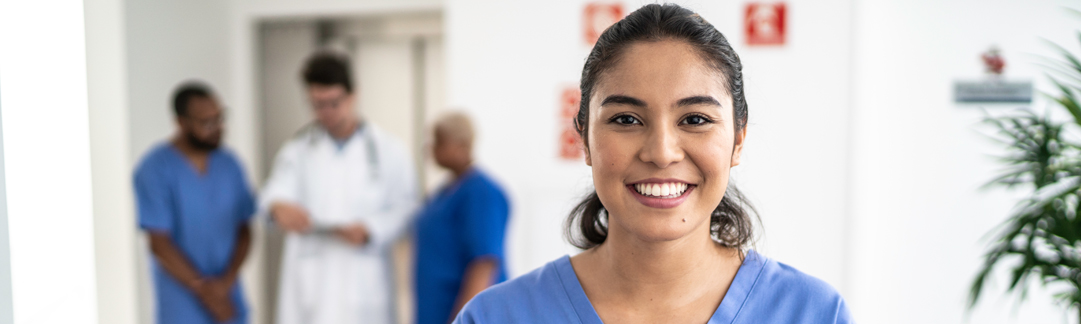 Newly graduated nurse smiling in front of other collaborating healthcare professionals.