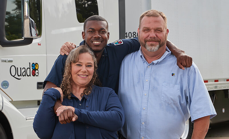 Three drivers smiling in front of a truck