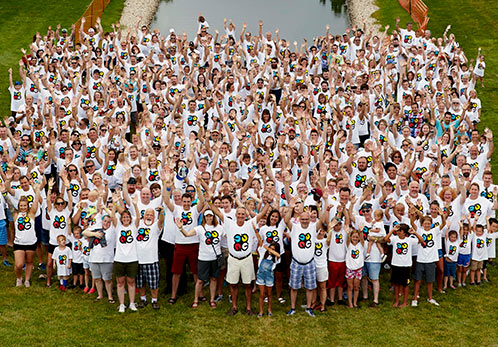 Dozens of Quad employees in a field at an outdoor event, cheering