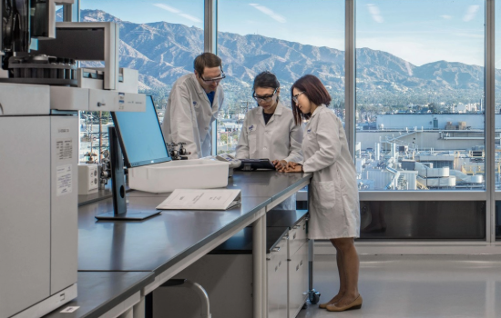 3 colleagues working together in a labratory setting with a large window overlooking the mountains