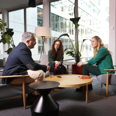 A group of colleagues seated in a lobby by a window having a conversation.