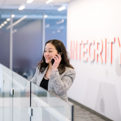 A smiling woman on the phone standing in front of a walk with the word "Integrity' emblazoned on it.
