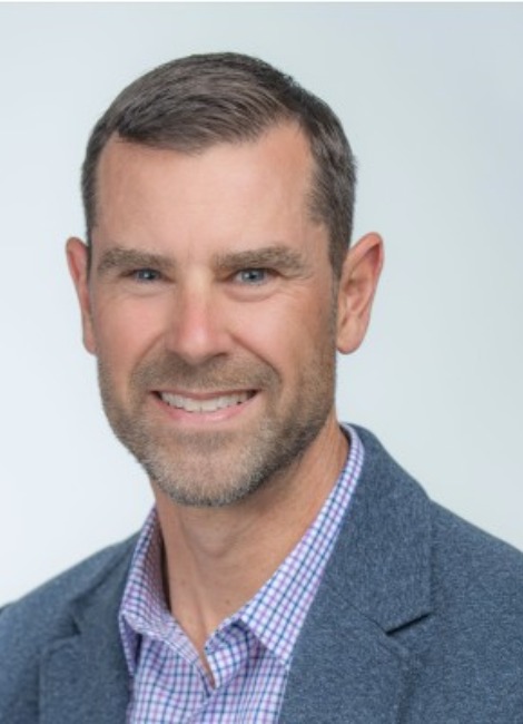 A professional headshot of a man, Jim Hansen, in a blue collared shirt with a blue jacket
