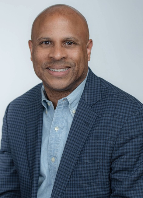 Professional headshot of a man, Ken Curtis, smiling in a collared shirt and suit jacket