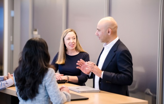 colleagues standing around a table listening intently to a man speaking