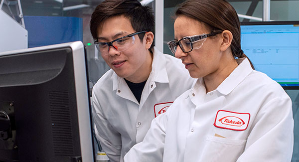 Two Takeda employees in lab coats and goggles