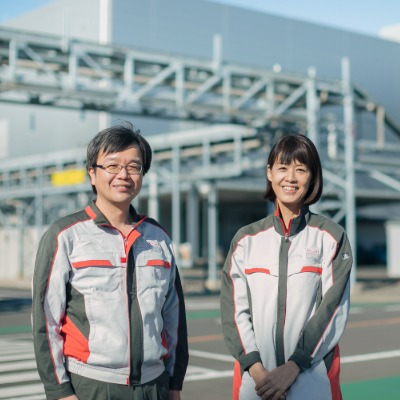 A male and female employee smiling and standing outside of a manufacturing facility on a sunny day