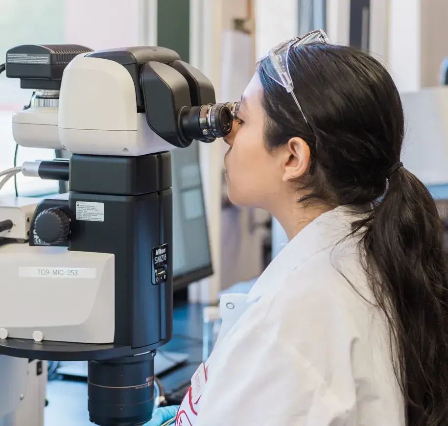 Woman in lab coat looking into a microscope