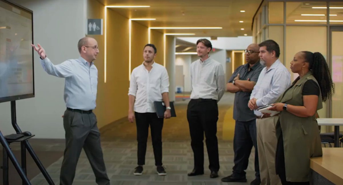 Watch video: Man pointing at a screen speaking to a group of people