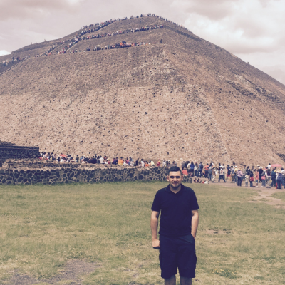 A man in black shorts and t-shirt standing on grass in front of a mountain