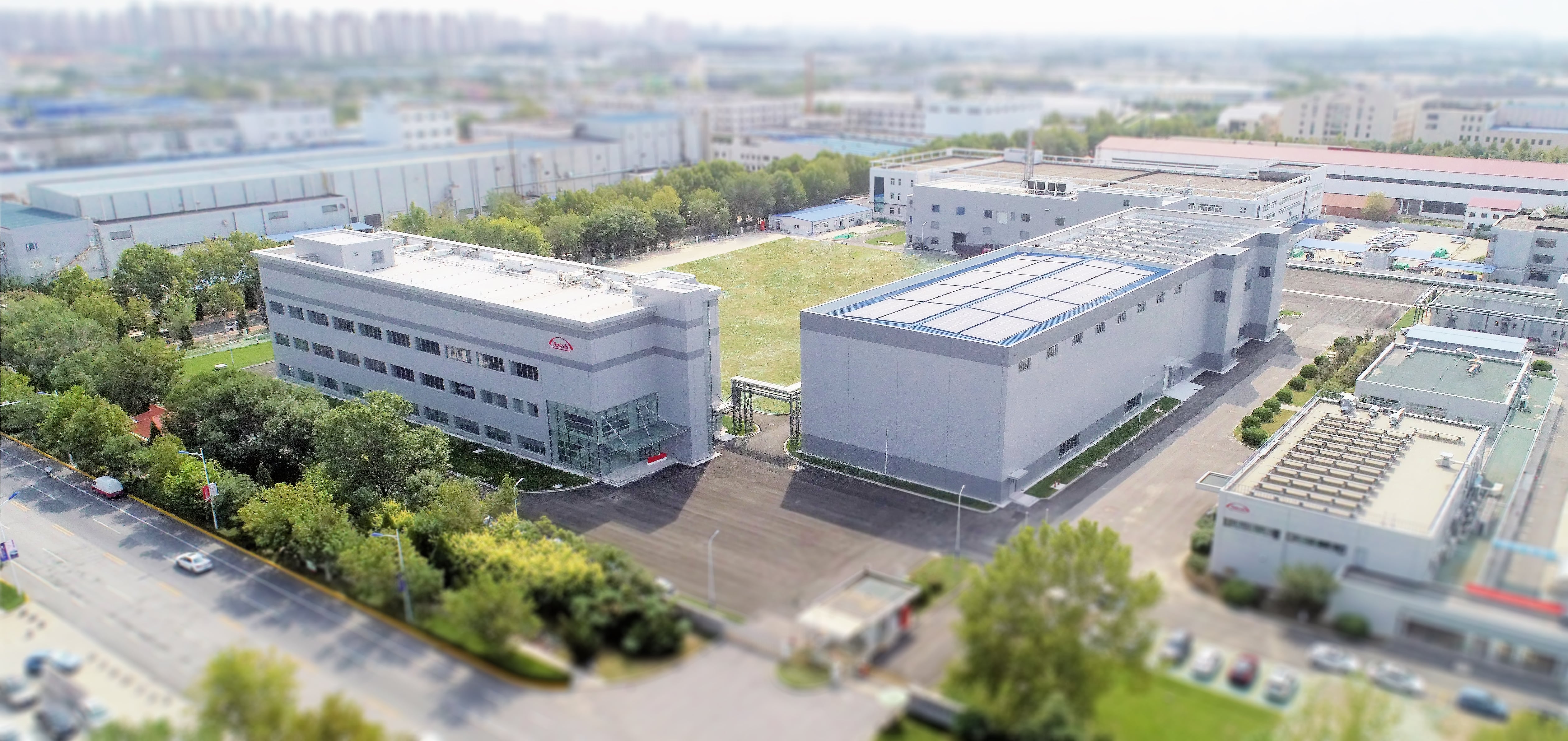 An aerial drone photo of 2 large factory buildings surrounded by trees