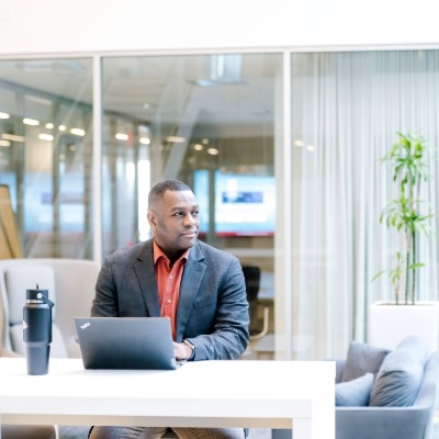 man seated at table alone in front of his computer look to the side in thought