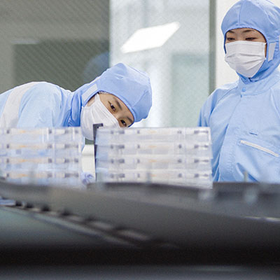Lab workers looking at items on conveyor belt while dressed in sterile clothing