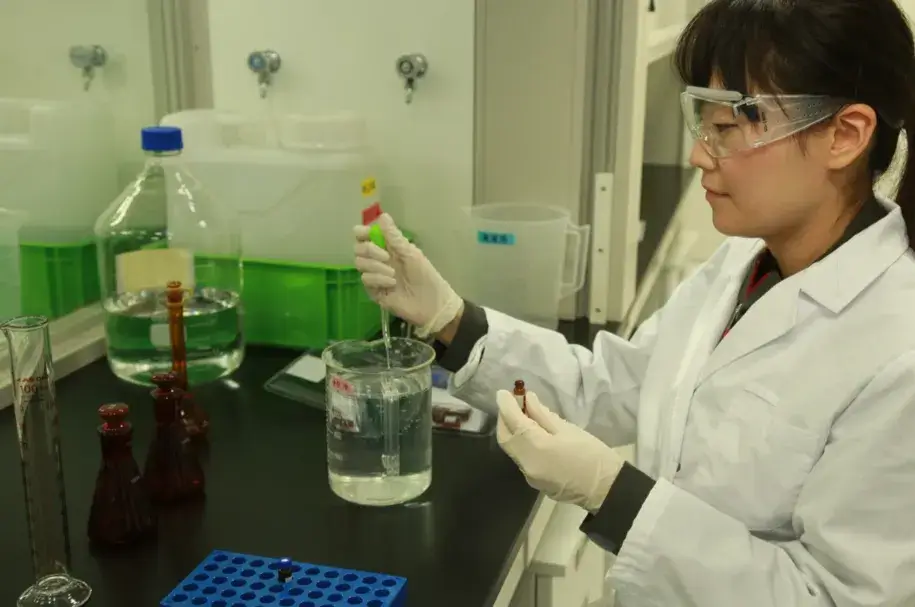 Woman in lab coat and safety glasses uses pipette in lab