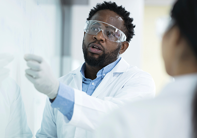 female employee in protective lab gear holding a binder and smiling