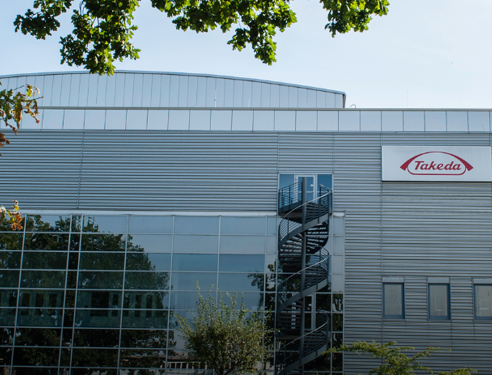 Large building with red Takeda logo surrounded by green trees