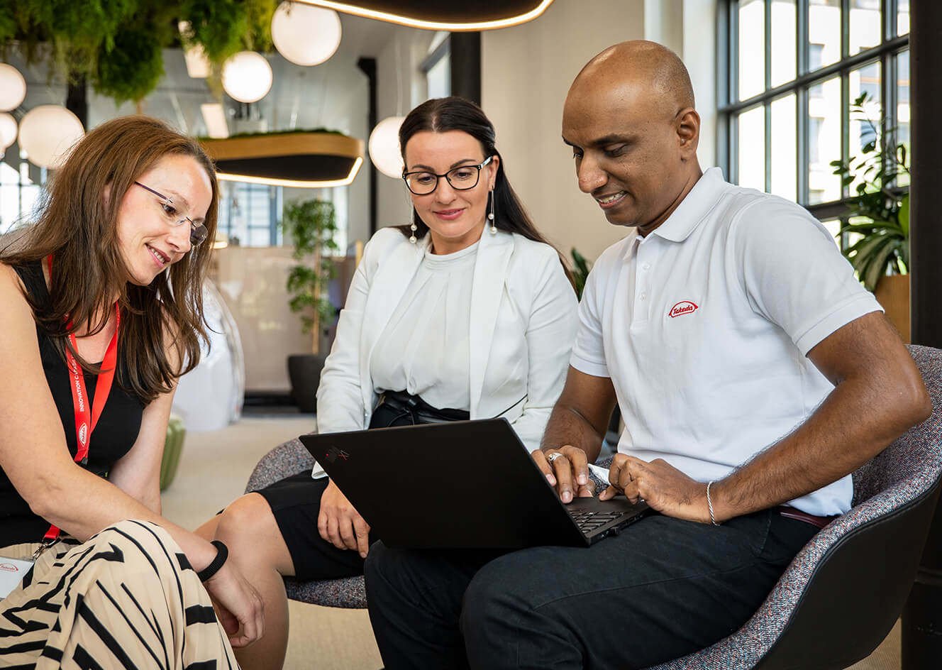 3 coworkers in business attire, sitting and looking at laptop screen together