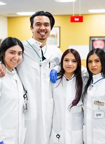 4 coworkers in lab coats smiling for a photo