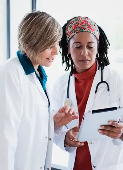 2 female persons in lab coats looking at a clipboard together