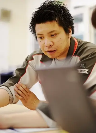 young asian male person seated behind a laptop