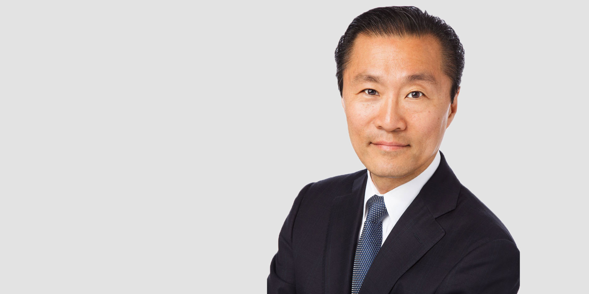 "Don Liu, in a dark suit and tie, looks at the camera against a grey background."