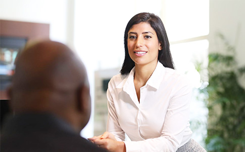  A pair of employees chatting over the edge of a desk in an open office, smiling 