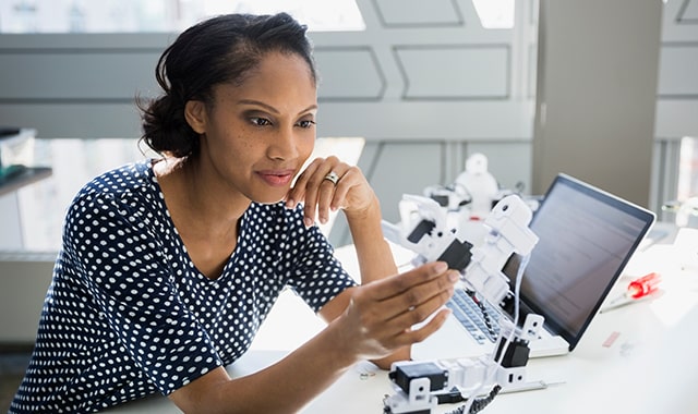 Young woman examining robotic arm at desk