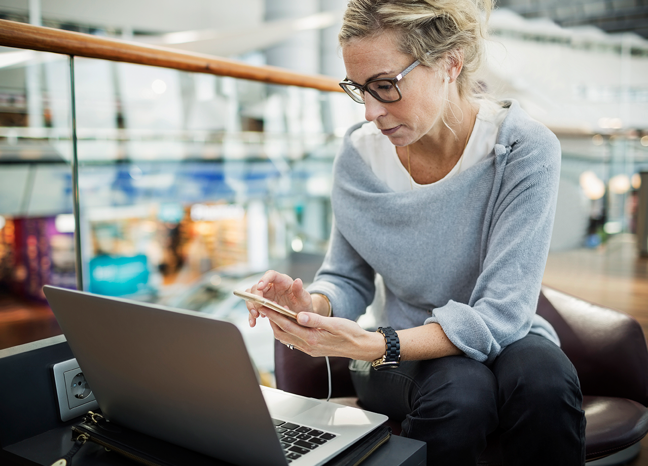 Employee using a laptop and smartphone while working in a modern office environment.