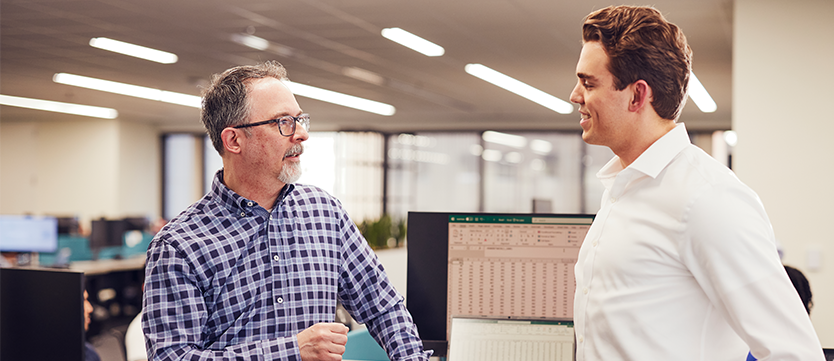 Two employees discussing work in a modern office near computer workstations.