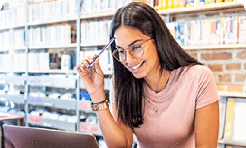 Hispanic female looking at something on the laptop while holding a pen against her head