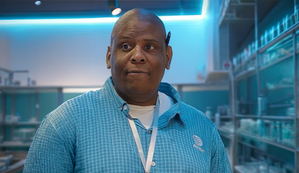 Person standing in a modern workspace wearing a blue shirt and lanyard.