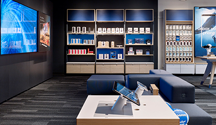 Interior of a mobile phone store featuring display shelves stocked with devices and accessories, interactive demo stations, and customer seating.