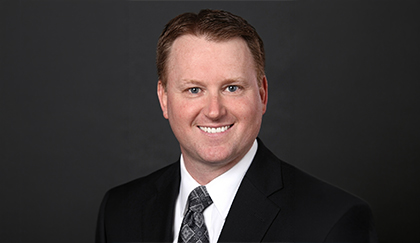 Professional headshot of a person in business attire against a dark background.