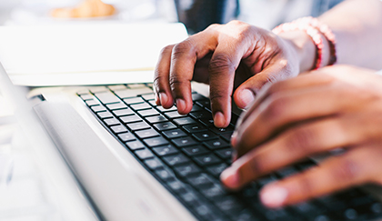 Close-up view of hands actively typing on a laptop computer keyboard in a workspace setting.