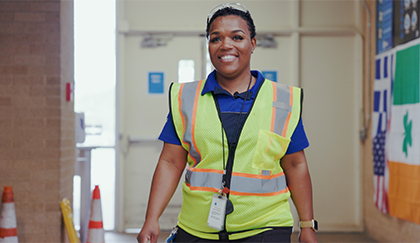 Person wearing a high-visibility safety vest and ID badge walking through a workplace hallway.