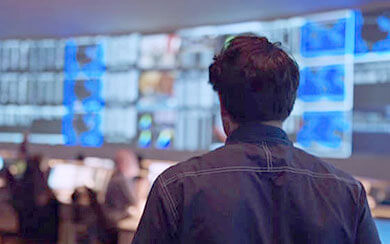 Male employee looking at a large wall filled with several computer screens