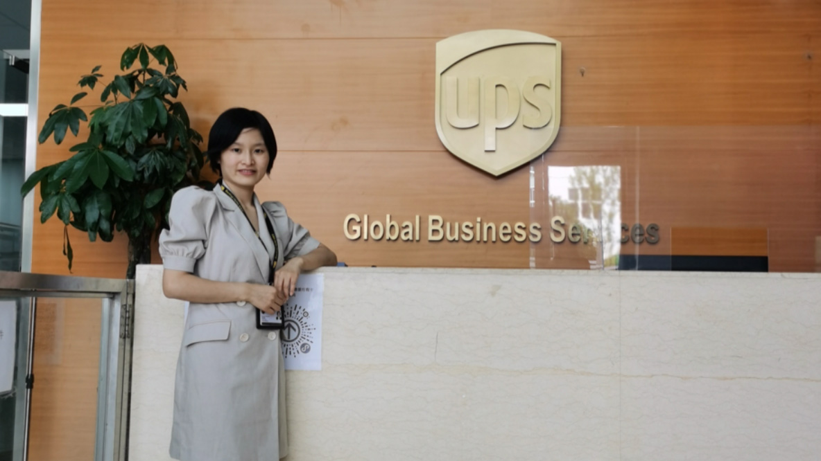 A woman standing in a reception area, smiling in front of UPS signage