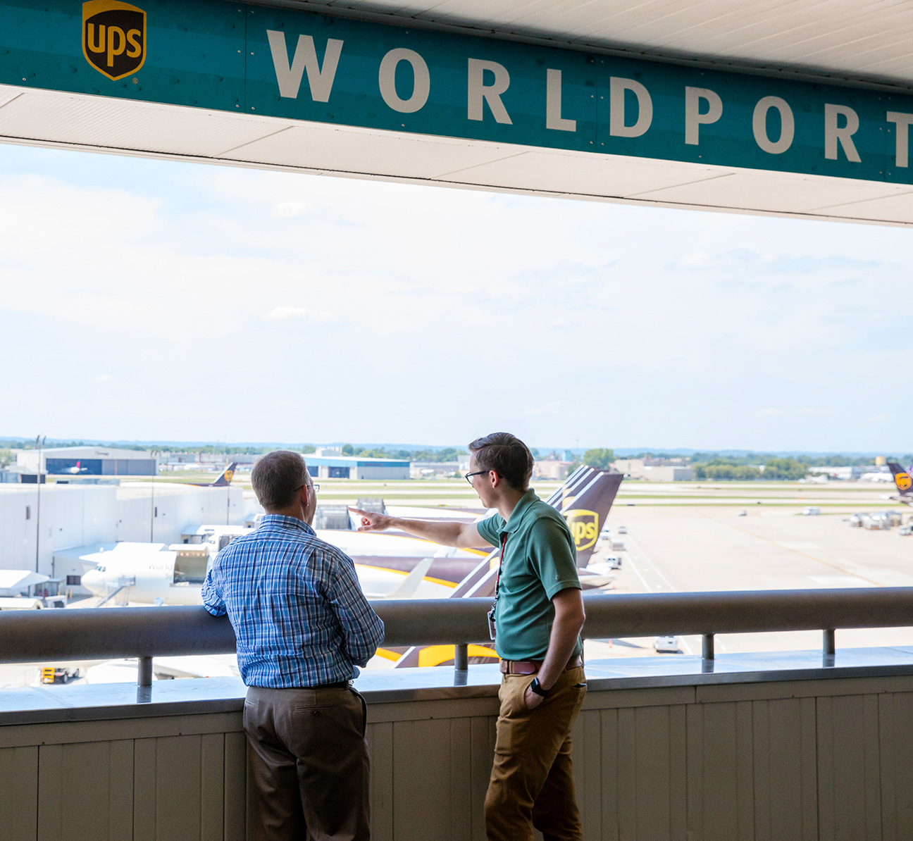Two people standing below a Worldport sign and overlooking UPS planes