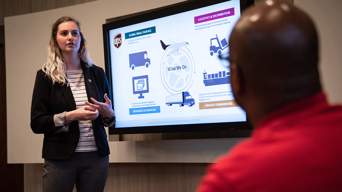 A woman standing in front of a large screen, presenting and speaking