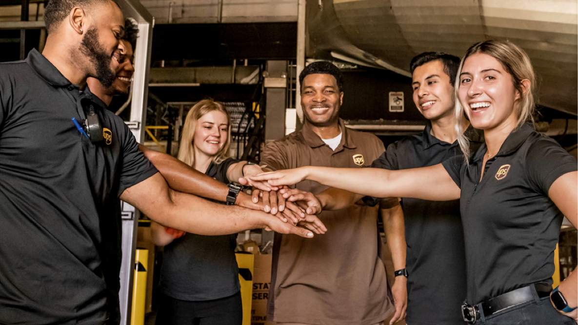 Six UPS employees putting their hands in together one on top of the other