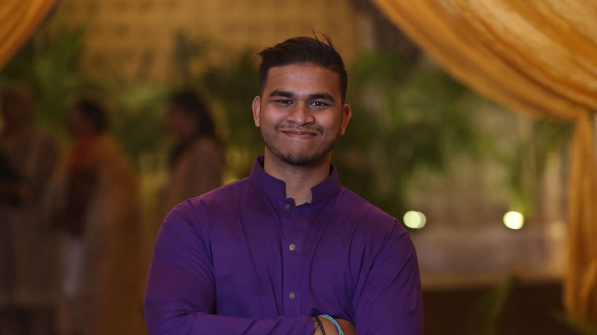 A man crossing his arms, wearing a purple shirt and smiling