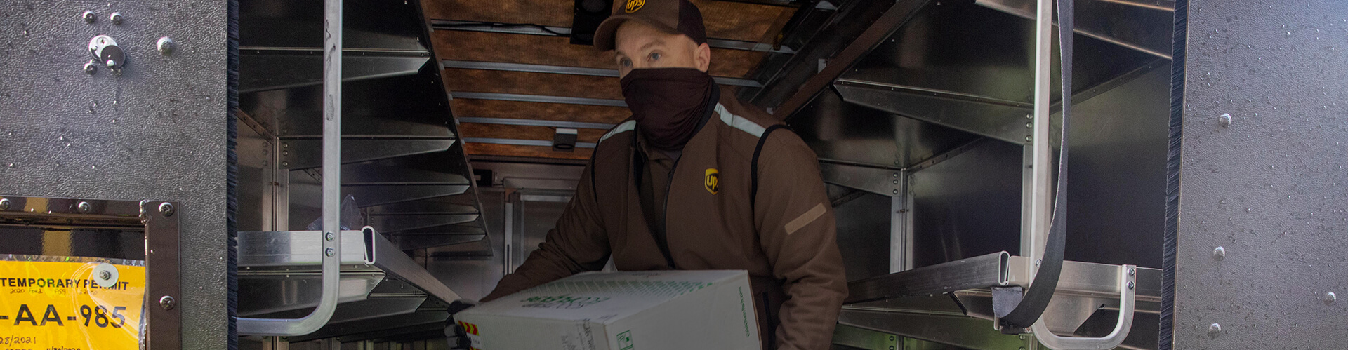 UPS employee wearing a mask while holding a container outside of a truck