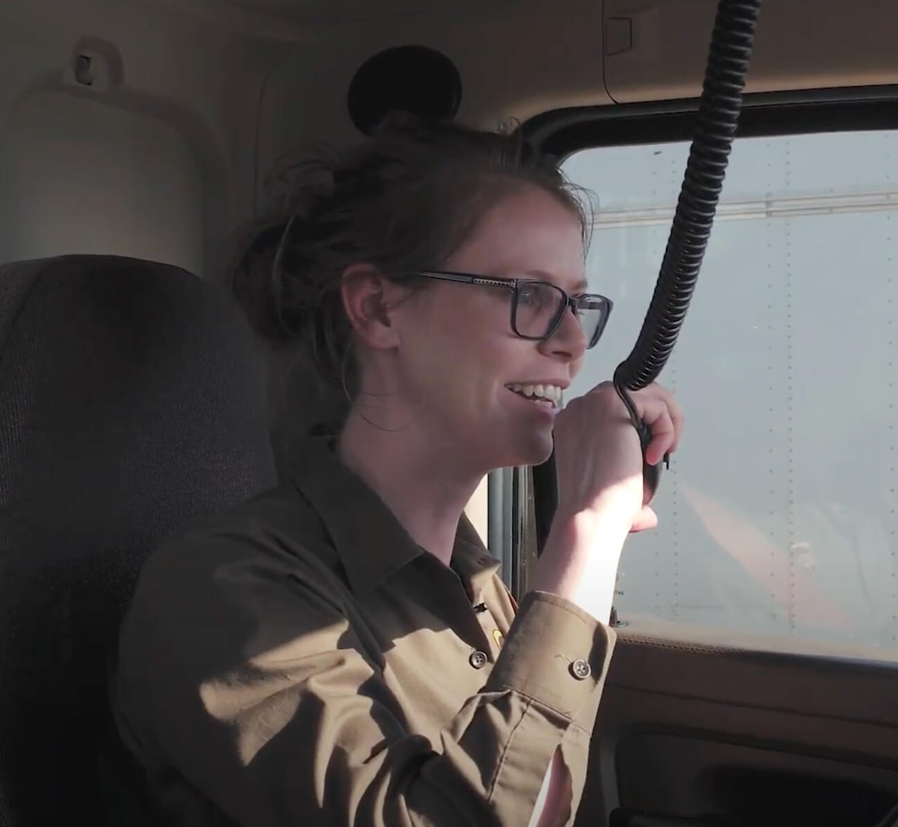 Olivia is smiling while talking on a truck radio