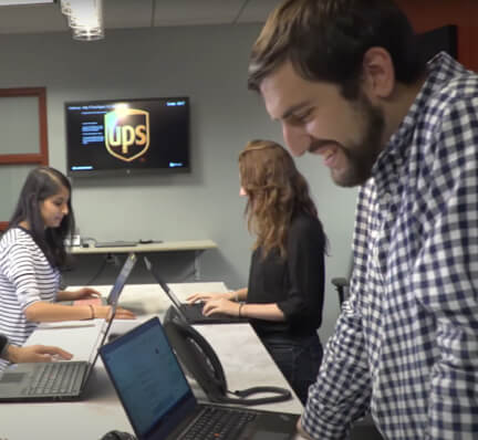 Several employees standing at a table together while working on laptops