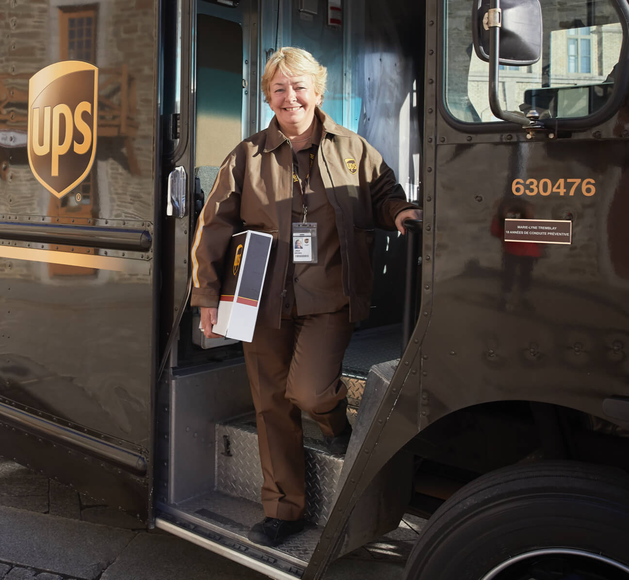 Female driver stepping out of a delivery truck and holding a package