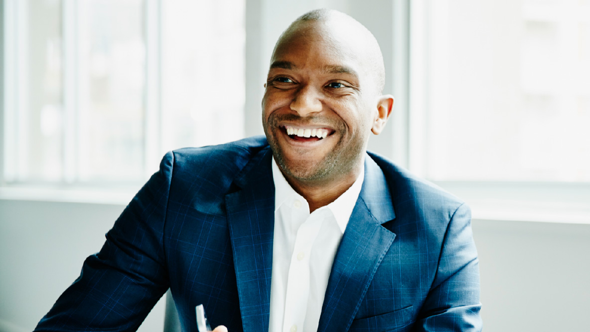 A man dressed in a suit, sitting and smiling