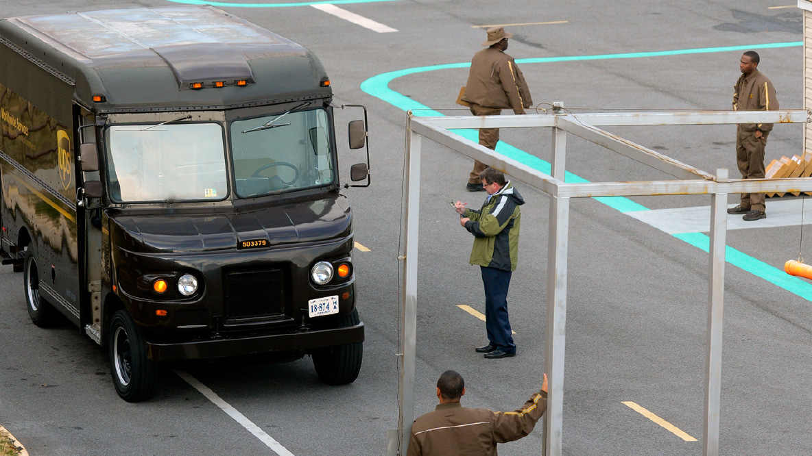 A group of UPS Drivers with a brown package delivery truck in a parking lot