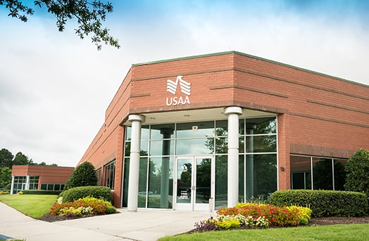 A stucco fronted building with high glass panels showing the entrance to the USAA office in Chesapeake, Virginia