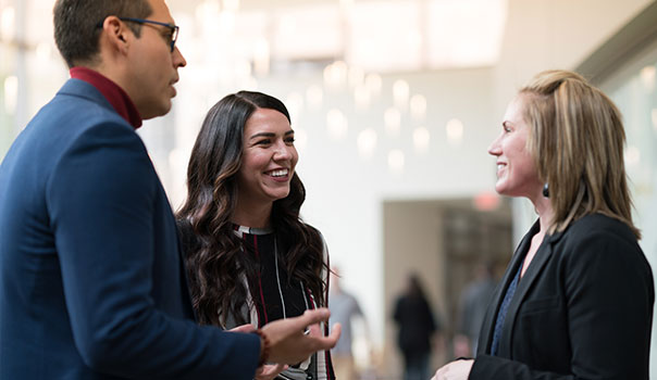 Two women and one man standing and talking to one another.